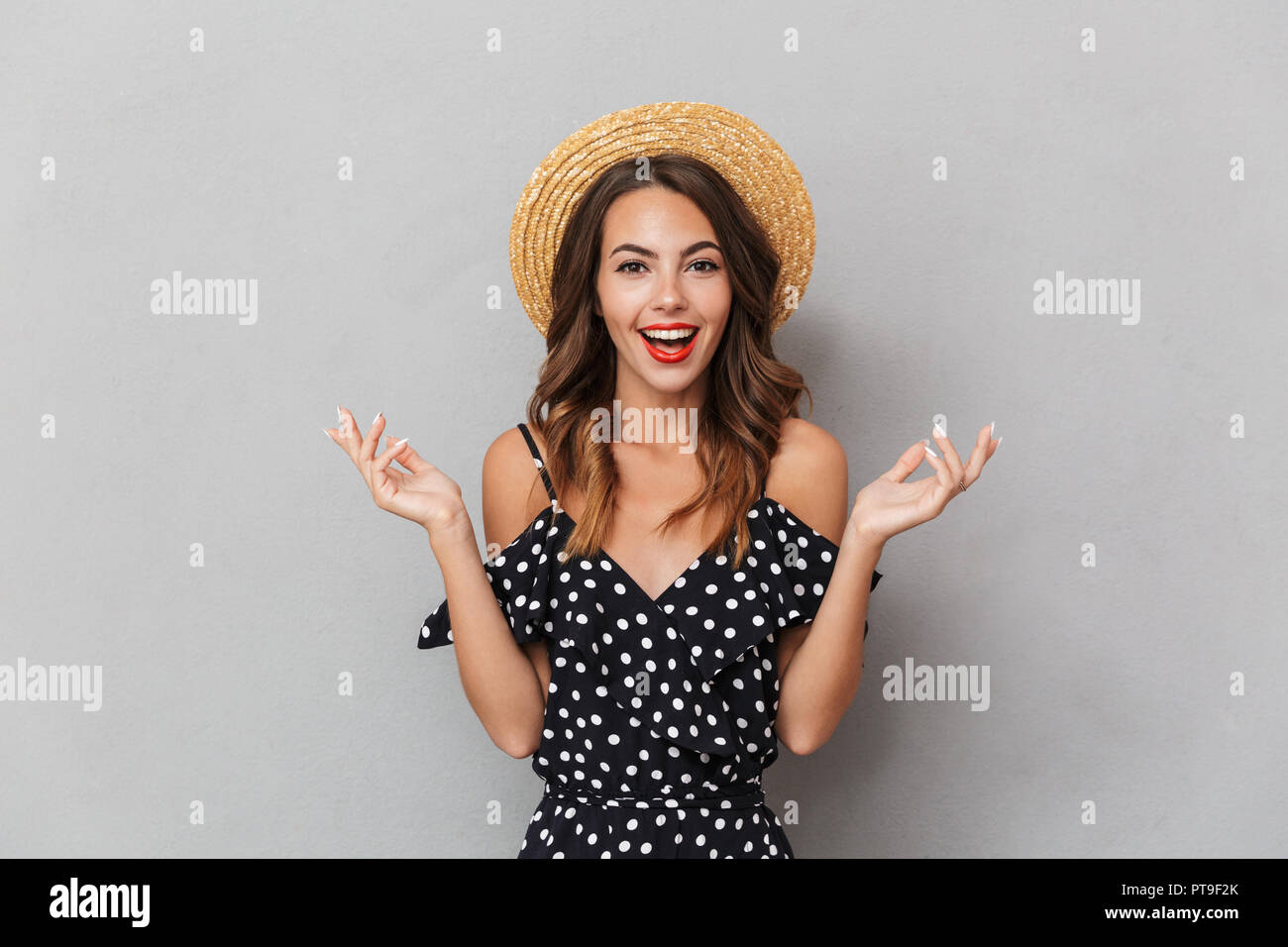 Portrait of a cheerful young girl in dress and straw hat over gray ...