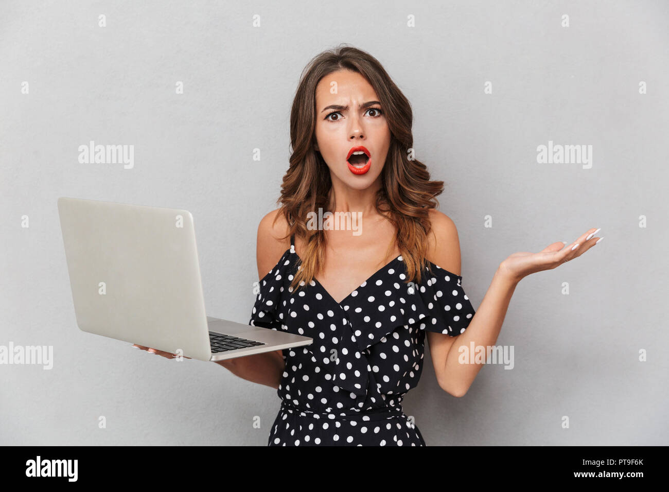 Portrait of a confused young girl in dress over gray background ...