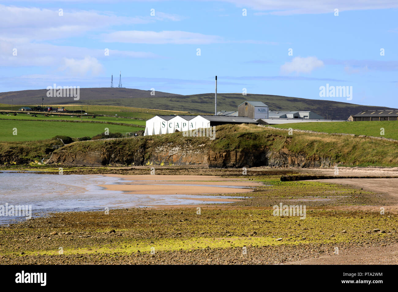 Scapa Bay near Kirkwall in Orkney with the Scapa distillery buildings sitting above the shoreline in the distance, Orkney, Scotland, Highlands, United Stock Photo