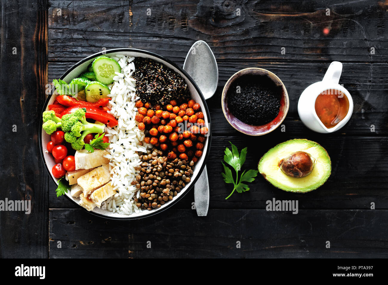 Buddha bowl. Clean and balanced healthy food concept. Rice, spicy chickpeas, black quinoa, vegetables and chicken fillet on dark wooden background, to Stock Photo
