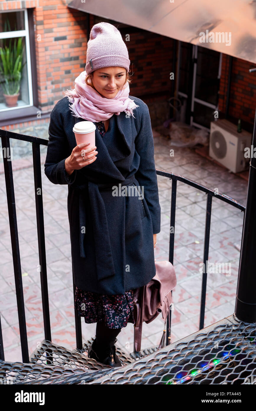 Coffee on the go. Stylish and young woman in coat and hat drinking