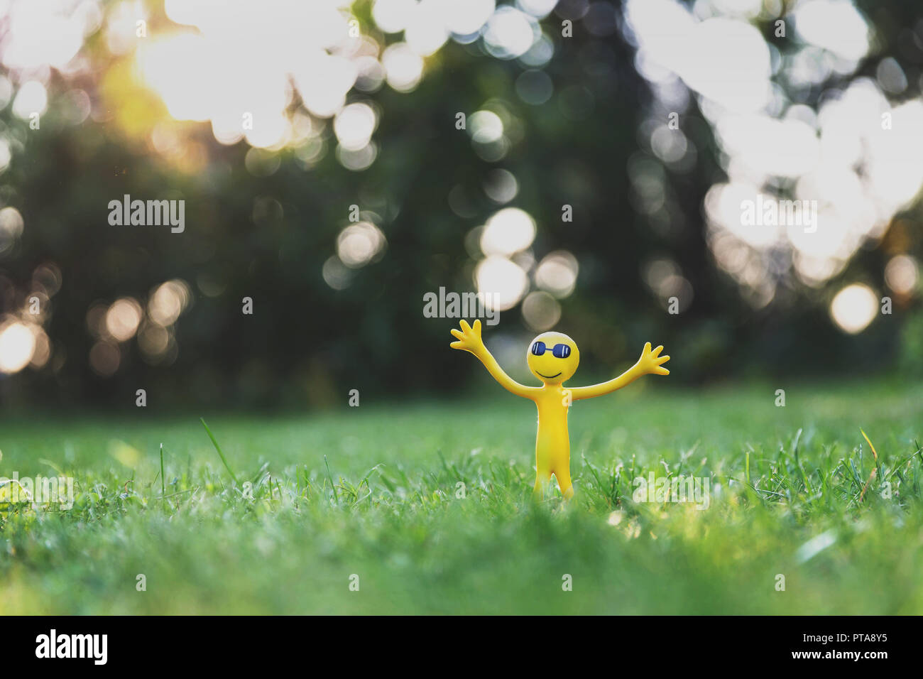 Funny little yellow guy with his hands up in the sunlight Stock Photo