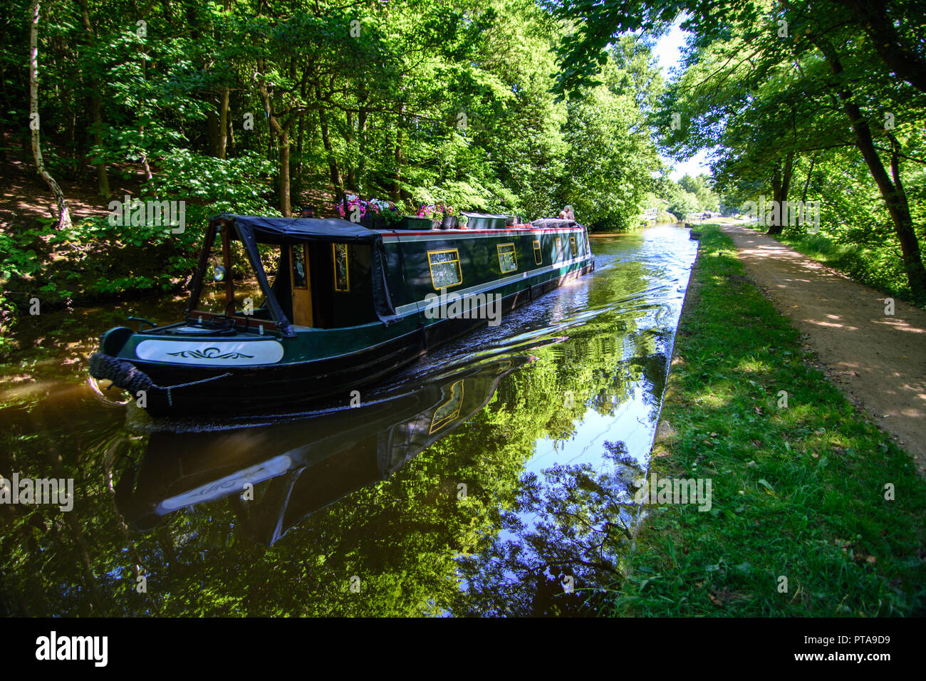 Shipley, England - June 30, 2015: A traditional narrowboat passes through the shade of woodland along the Leeds and Liverpool Canal at Shipley near Br Stock Photo