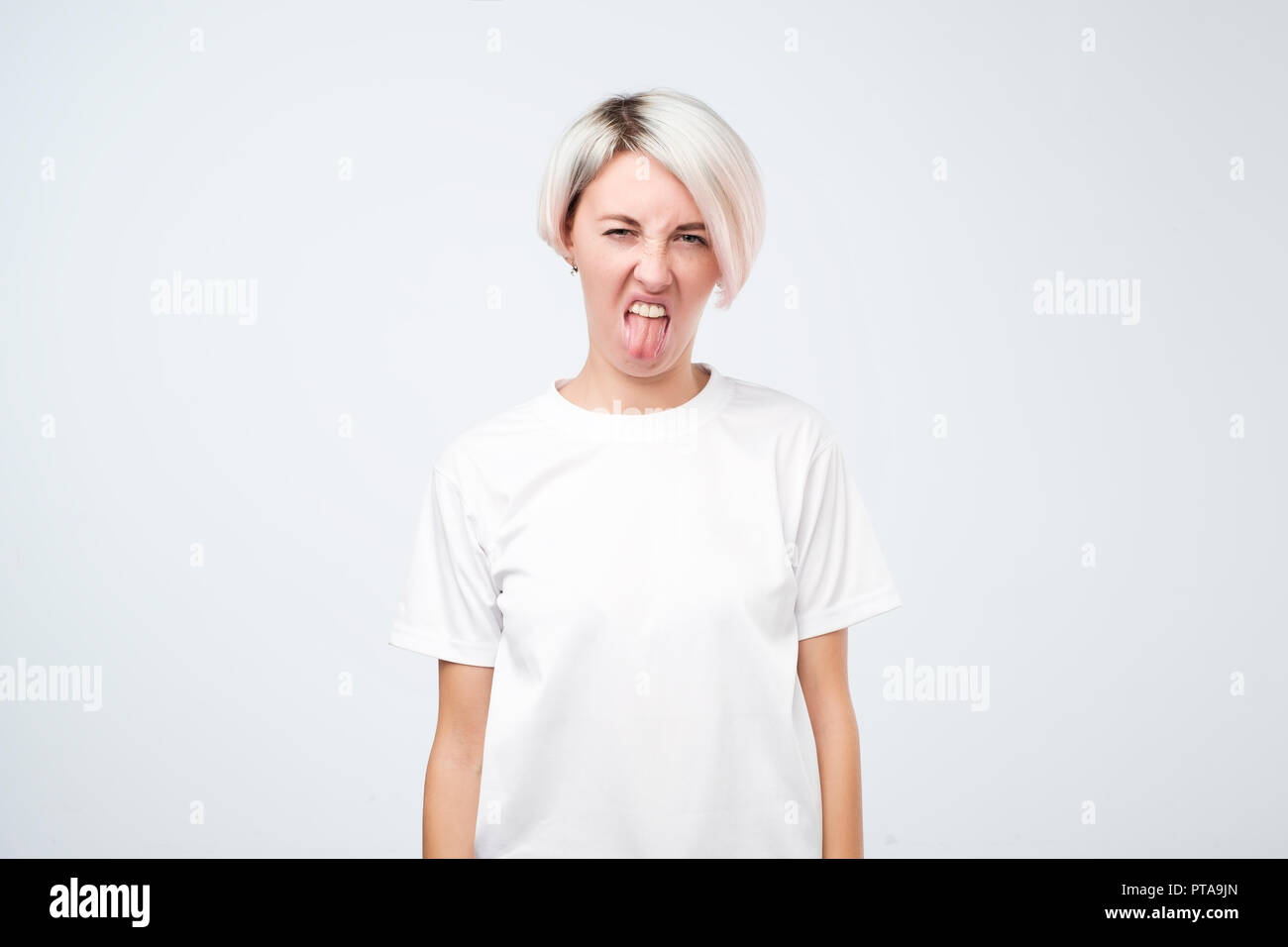 Teenager with short colored hairstyle frowns face, has disgusting expression, shows tongue Stock Photo