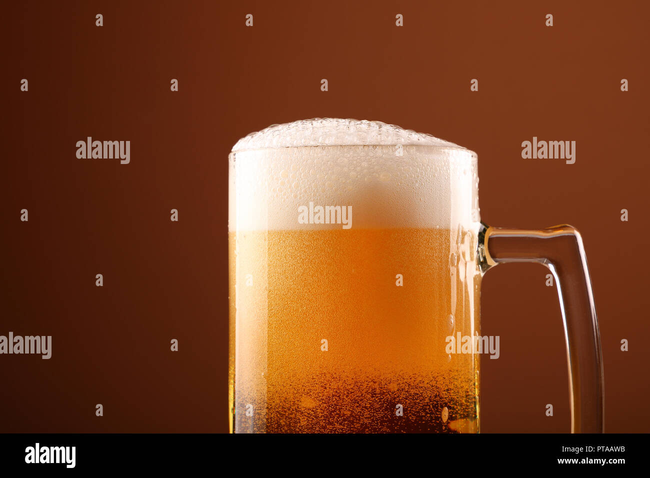 Close up pouring lager beer with white froth and bubbles in glass mug over dark brown background with copy space, low angle side view Stock Photo