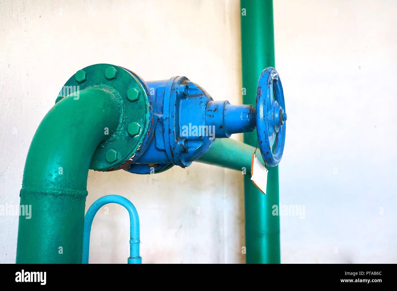 Old blue valve on the cold water pipeline painted green. Industrial background. Stock Photo