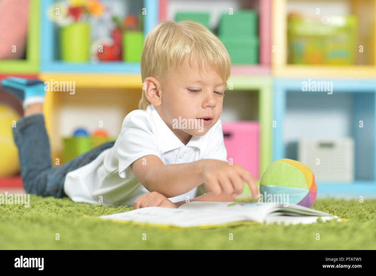 Portrait of cute little boy reading a book while lying on floor Stock ...