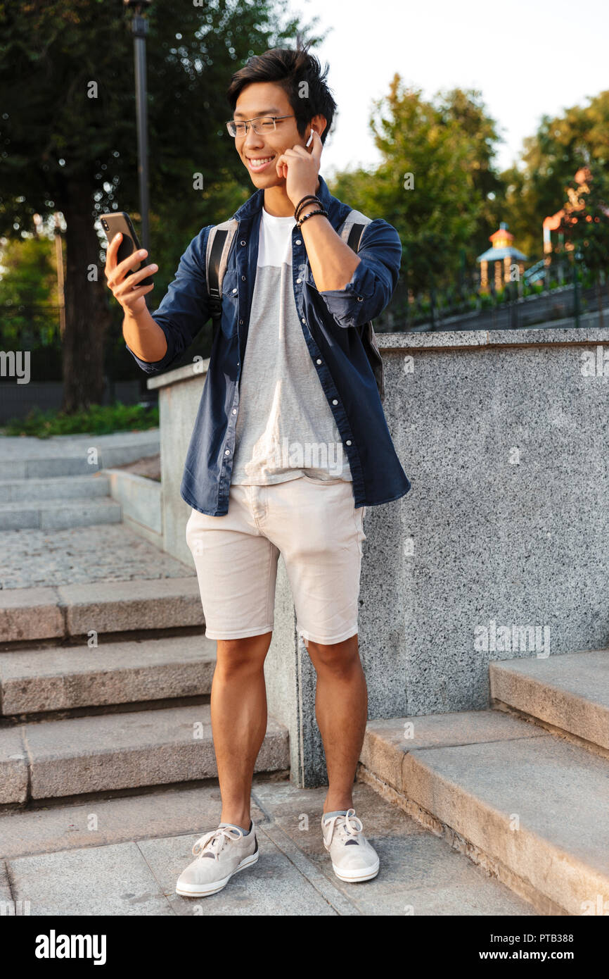 Full length image of Happy asian male student in eyeglasses talking by  video call on smartphone outdoors Stock Photo - Alamy