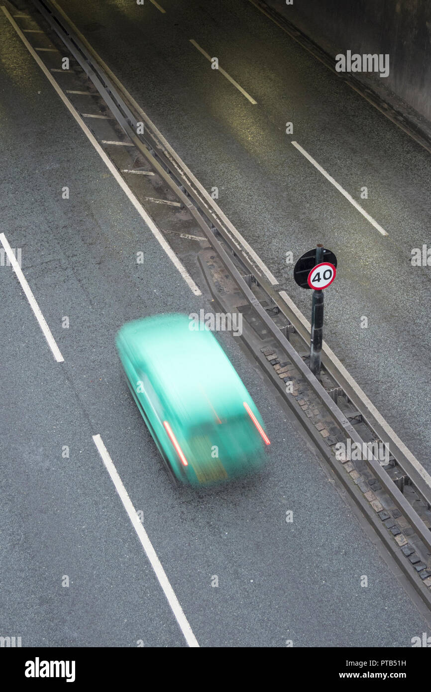 Small Green car passing a speed limit sign on a dual carriageway Stock