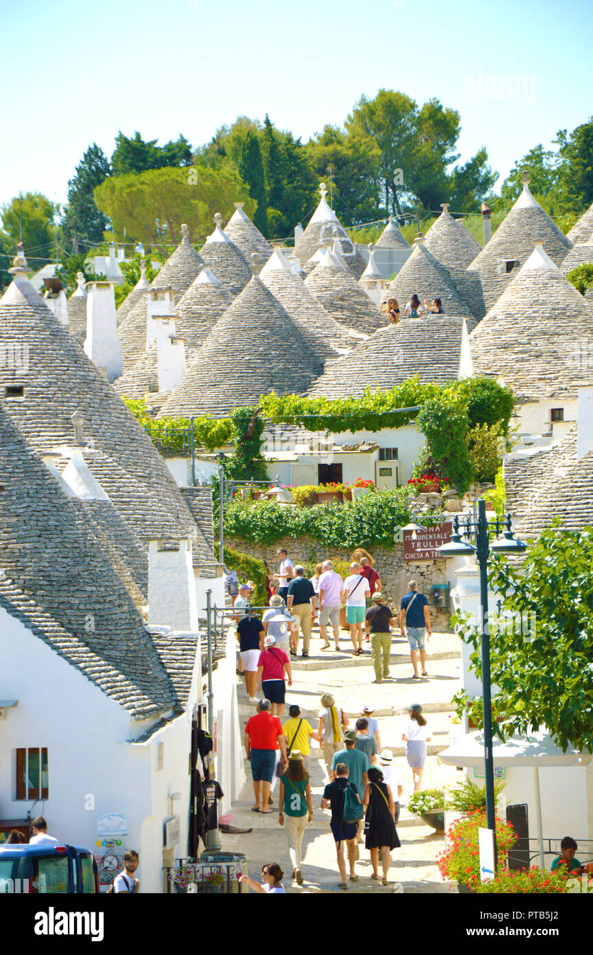 ALBEROBELLO, ITALY - JULY 31, 2017: Beautiful town of Alberobello with trulli houses among green plants and flowers, main touristic district, Apulia r Stock Photo