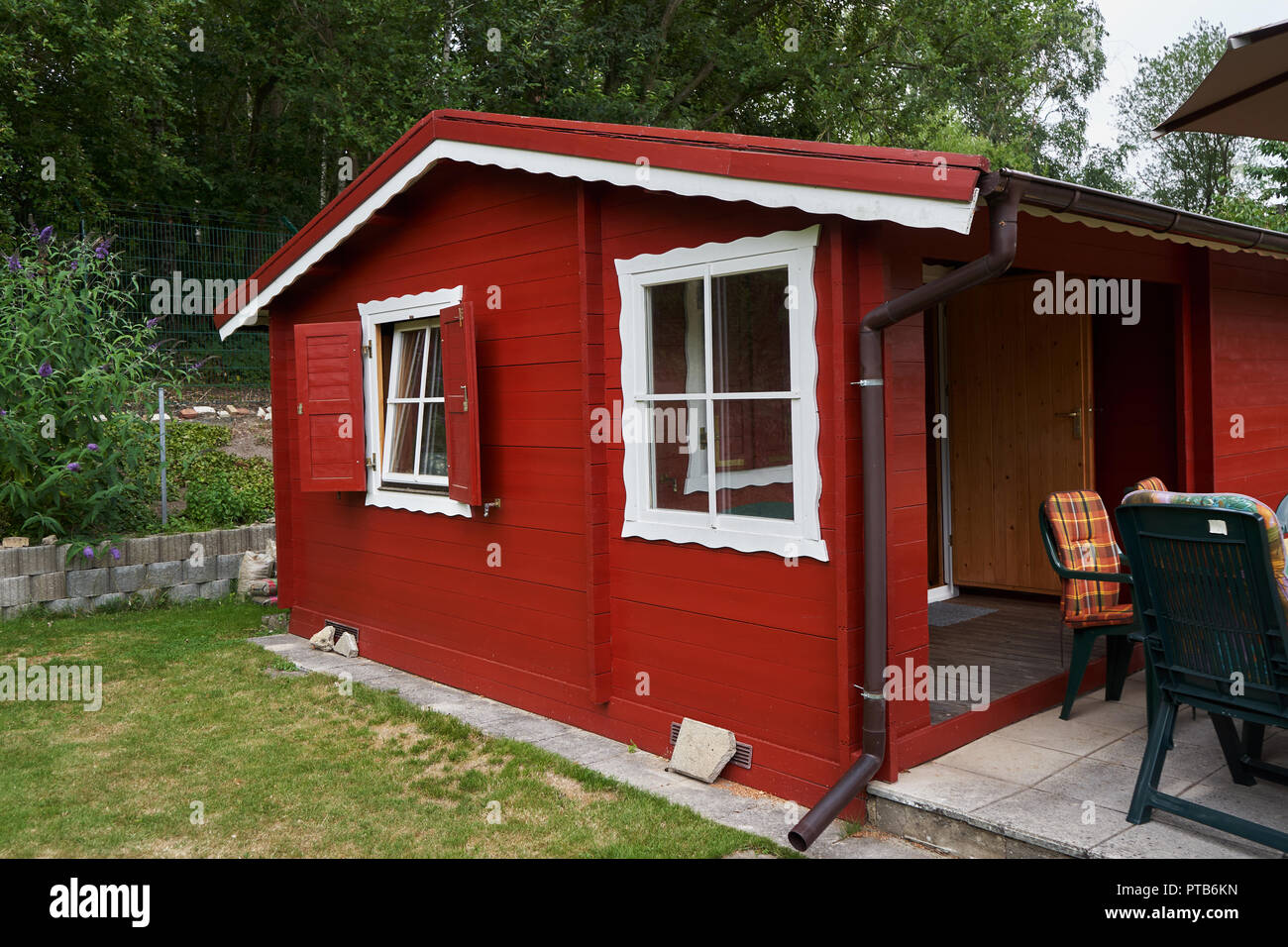 Small red painted garden house with patio and chairs and decorative white trim around the roof and windows. Stock Photo