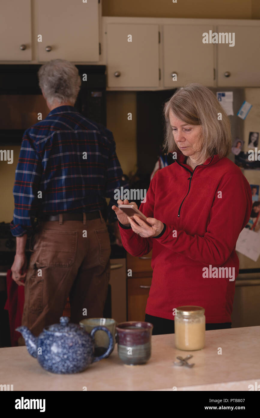 Senior woman using mobile phone while man working in background Stock Photo