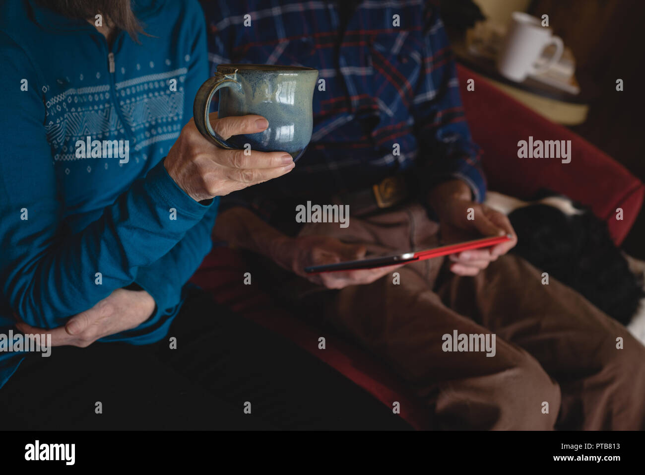 Senior couple using digital tablet while having coffee in living room Stock Photo