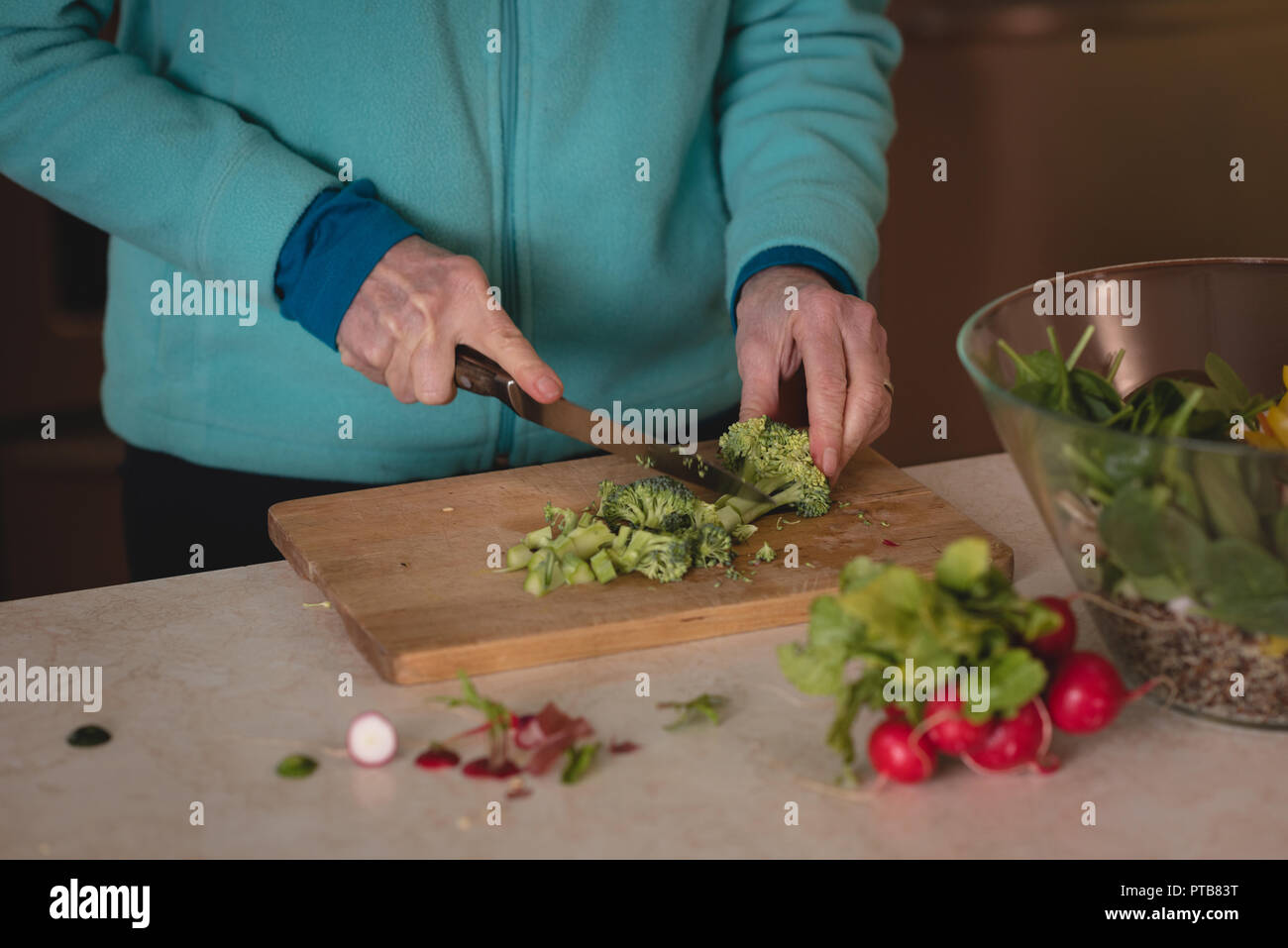 Woman chopping broccoli with knife on chopping board Stock Photo