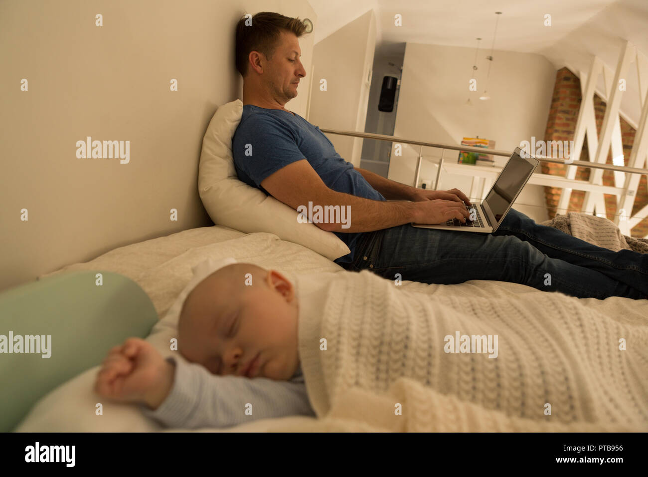 Baby boy sleeping while father using laptop in bedroom Stock Photo