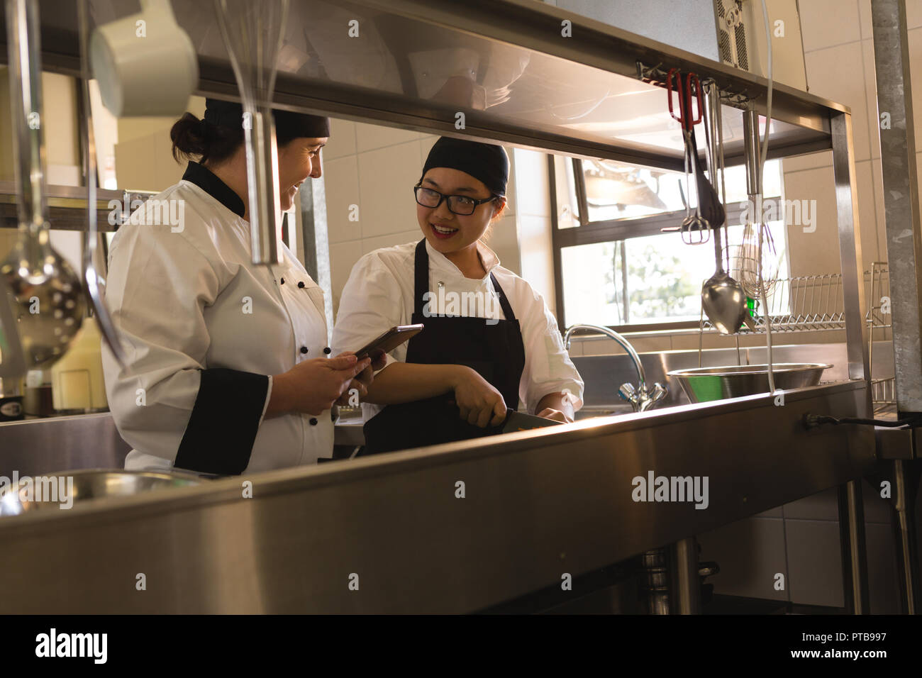 Two female chefs interacting with each other in kitchen Stock Photo