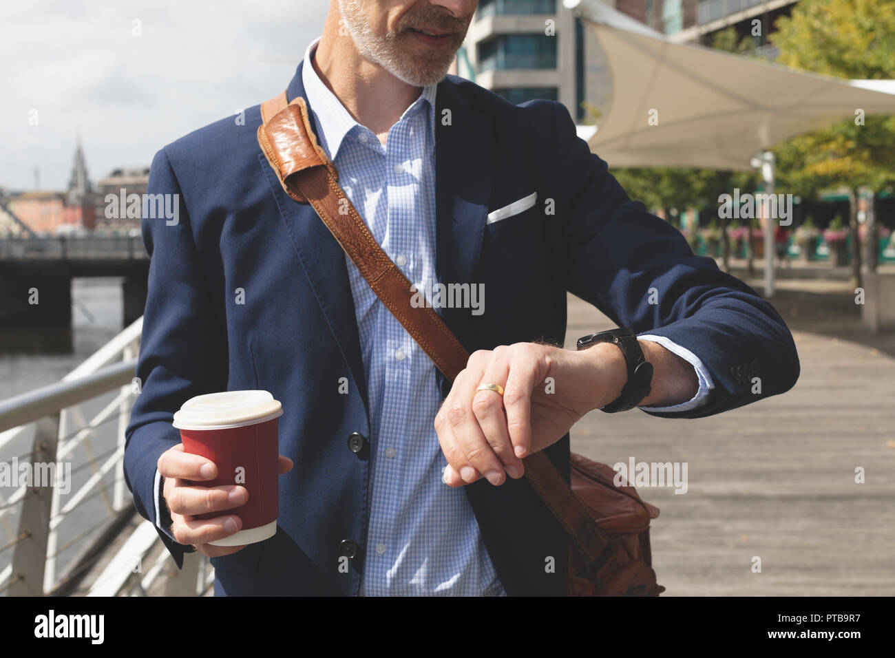Businessman checking time on smartwatch at promenade Stock Photo