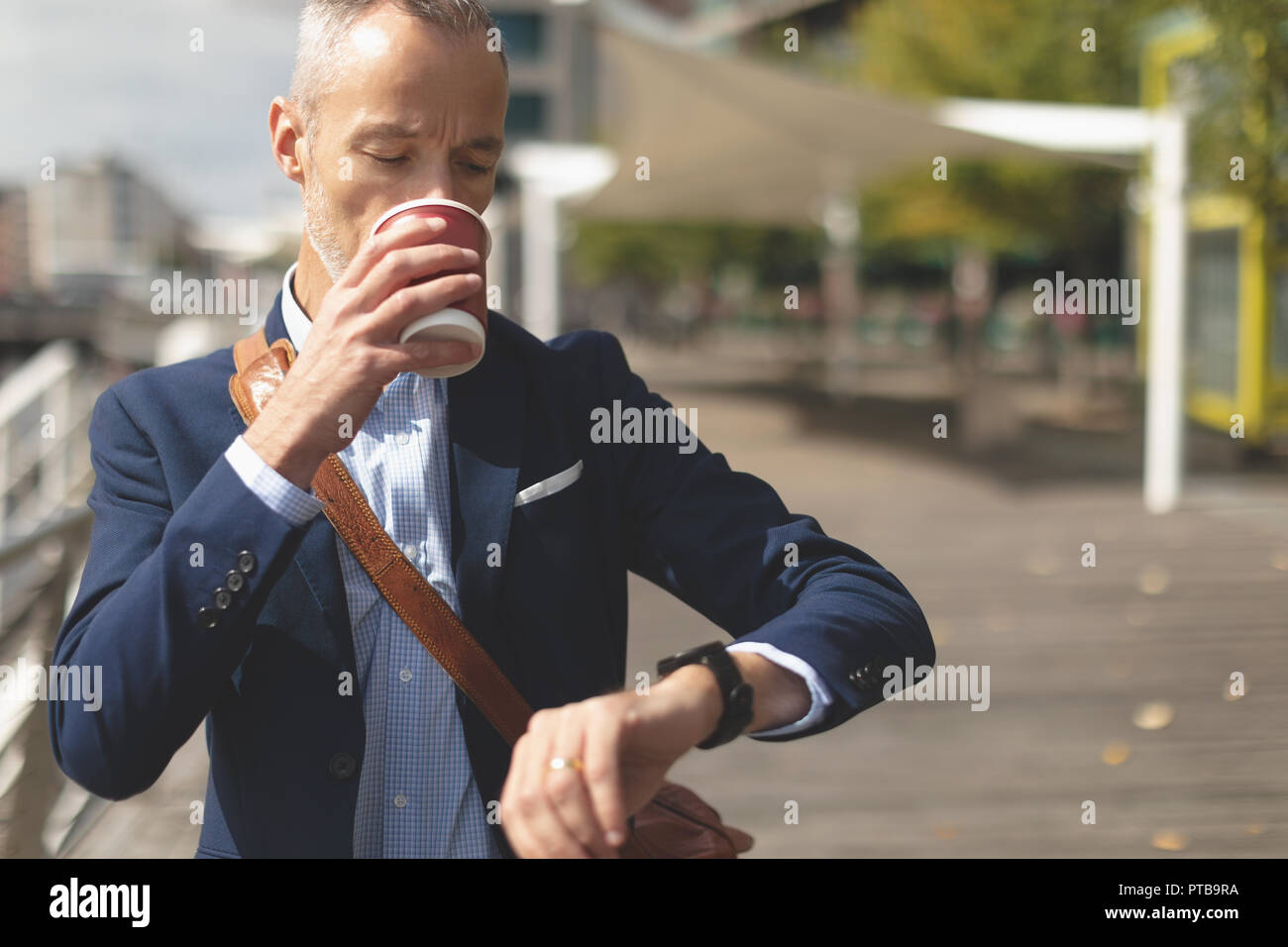 Businessman having coffee while checking time on smartwatch Stock Photo