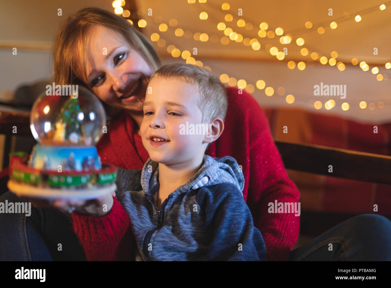 Mother and son holding Christmas tree snow globe at home Stock Photo