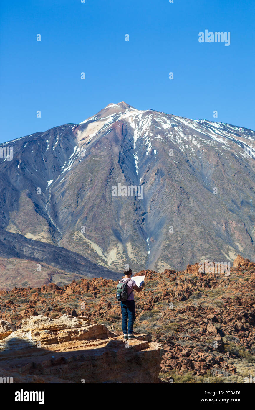 Lost hiker checks map to find directions standing on the edge of rock with volcano El Teide on background. National park of Tenerife, Canary Islands,  Stock Photo