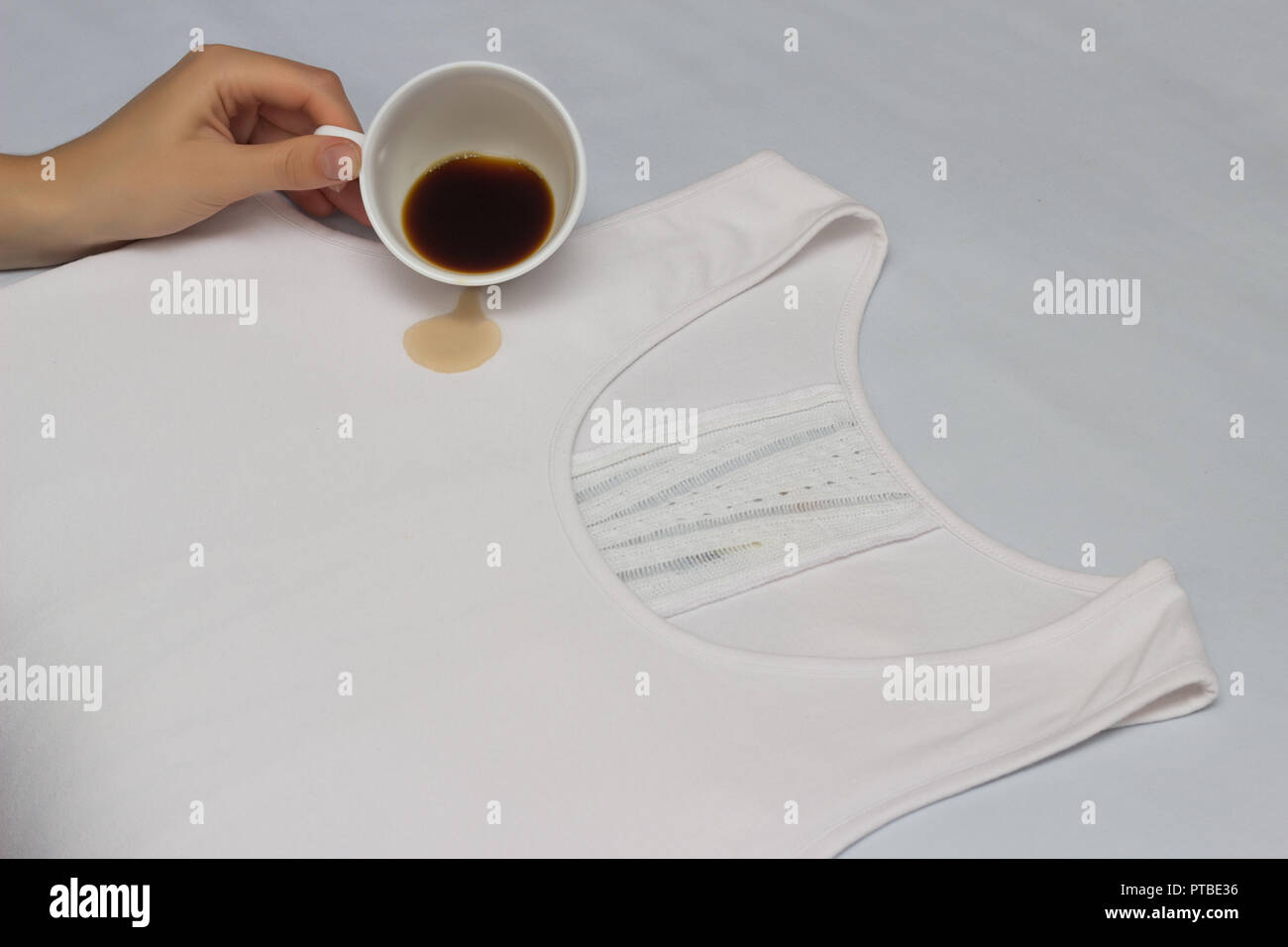 Girl pours a cup of coffee on a white jersey, fighting stains on clothes, checking stain remover, coffee and stain, close-up, hand, cup Stock Photo