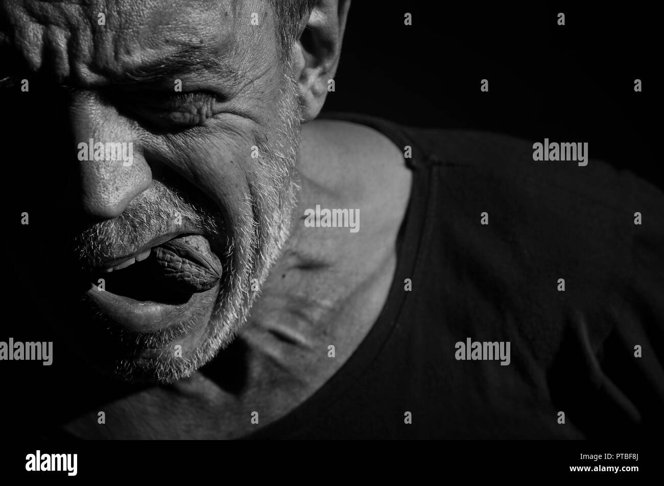 An elderly man is trying to get a nut through his teeth in black and white. Stock Photo