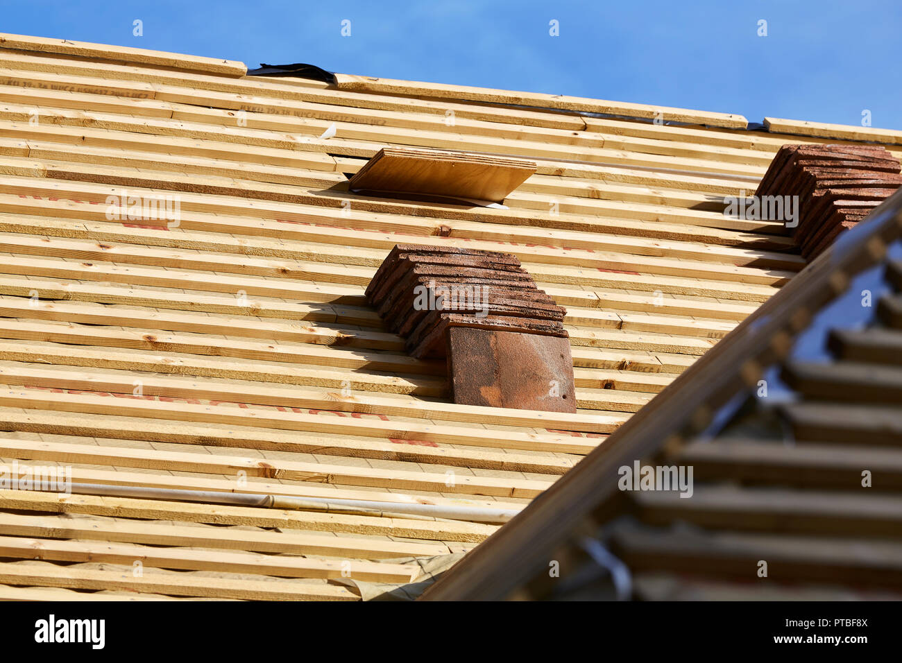 A number of roofing tiles stacked against tile batten on a roof waiting to be laid on an a new extension of a building Stock Photo