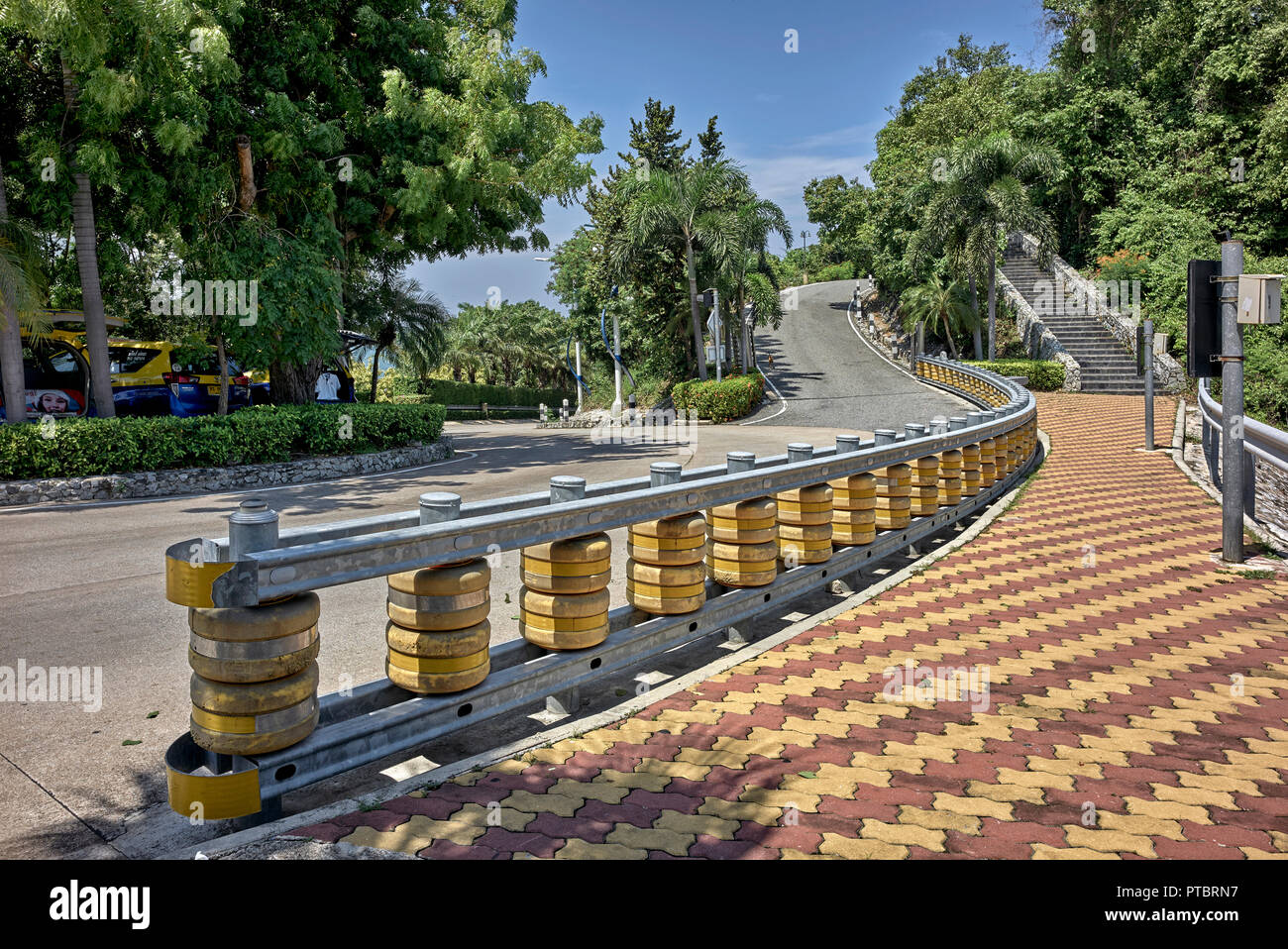 Crash barrier positioned at the foot of a steep hill with a dangerous bend and oncoming merging traffic Stock Photo