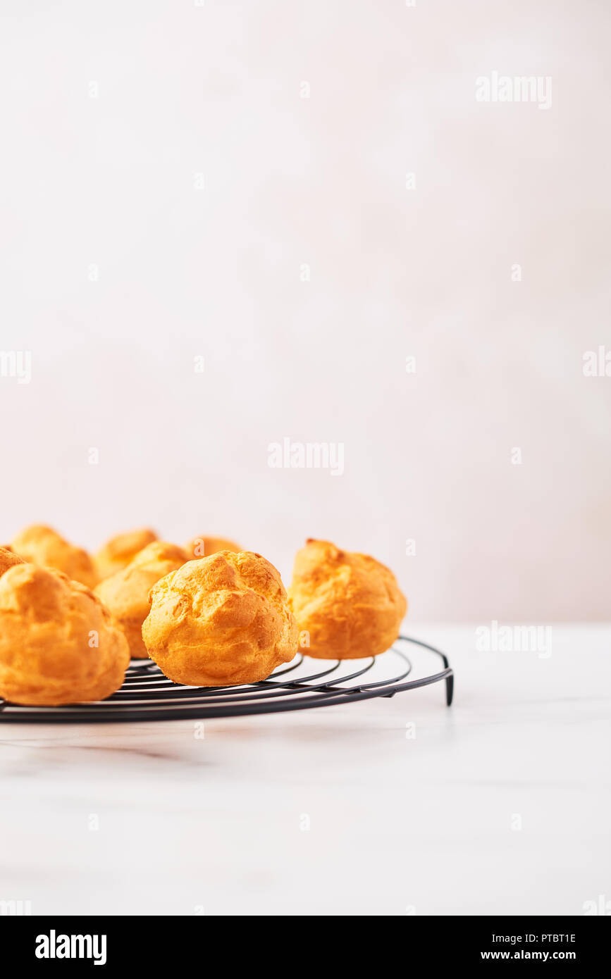 Bunch of fresh cream puff cakes on French wire rack on white marble table over pink background with copy space. Selective focus. Stock Photo
