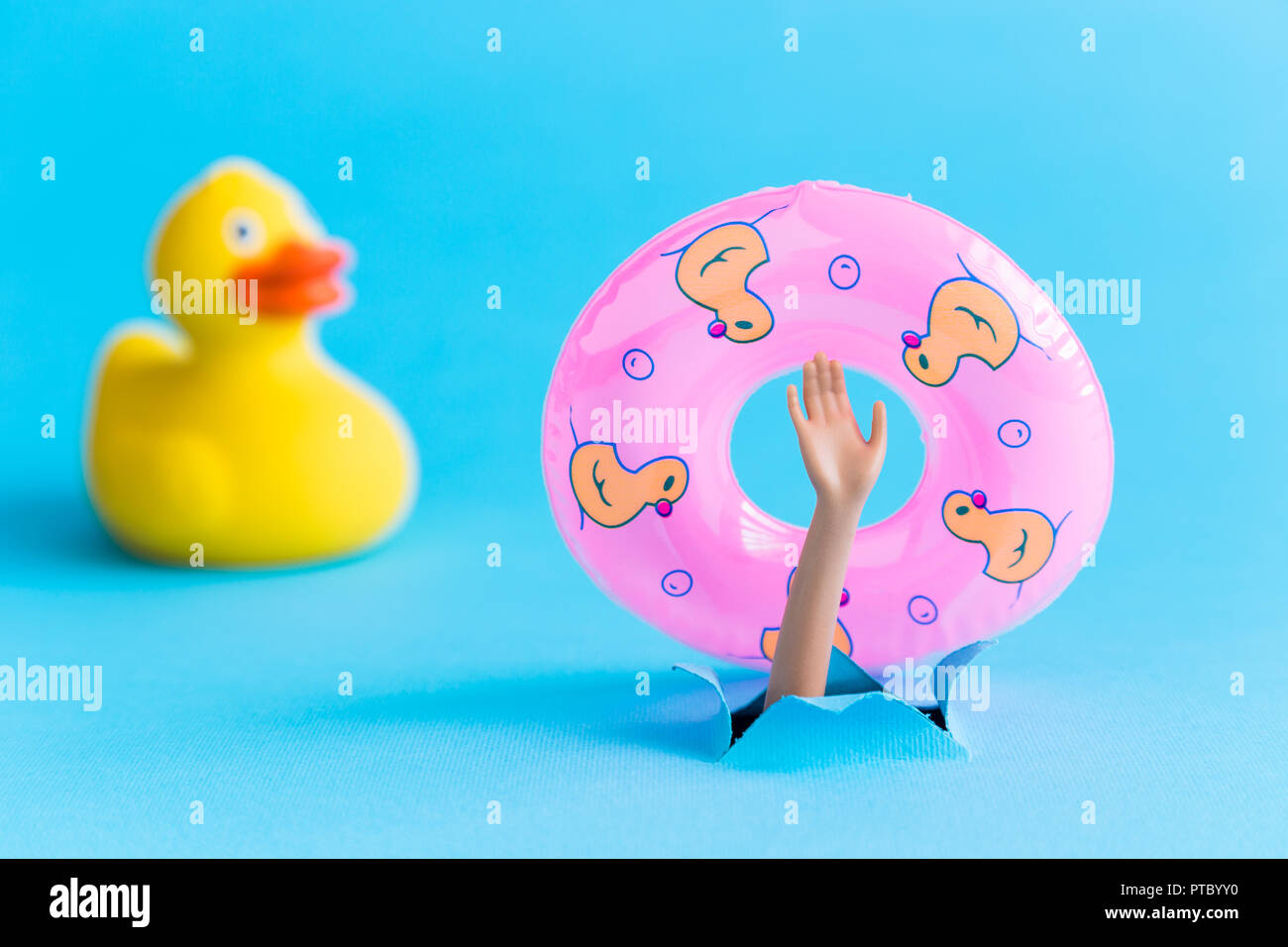 Small rubber duck and doll hand from the water with inflatable pool float minimalistic abstract. Stock Photo