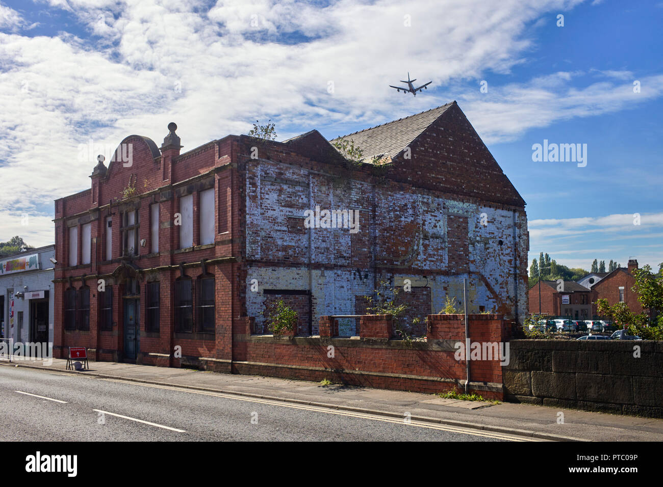 An airliner landing at Manchester airport passing over an abandoned and run down factory building in Stockport Stock Photo