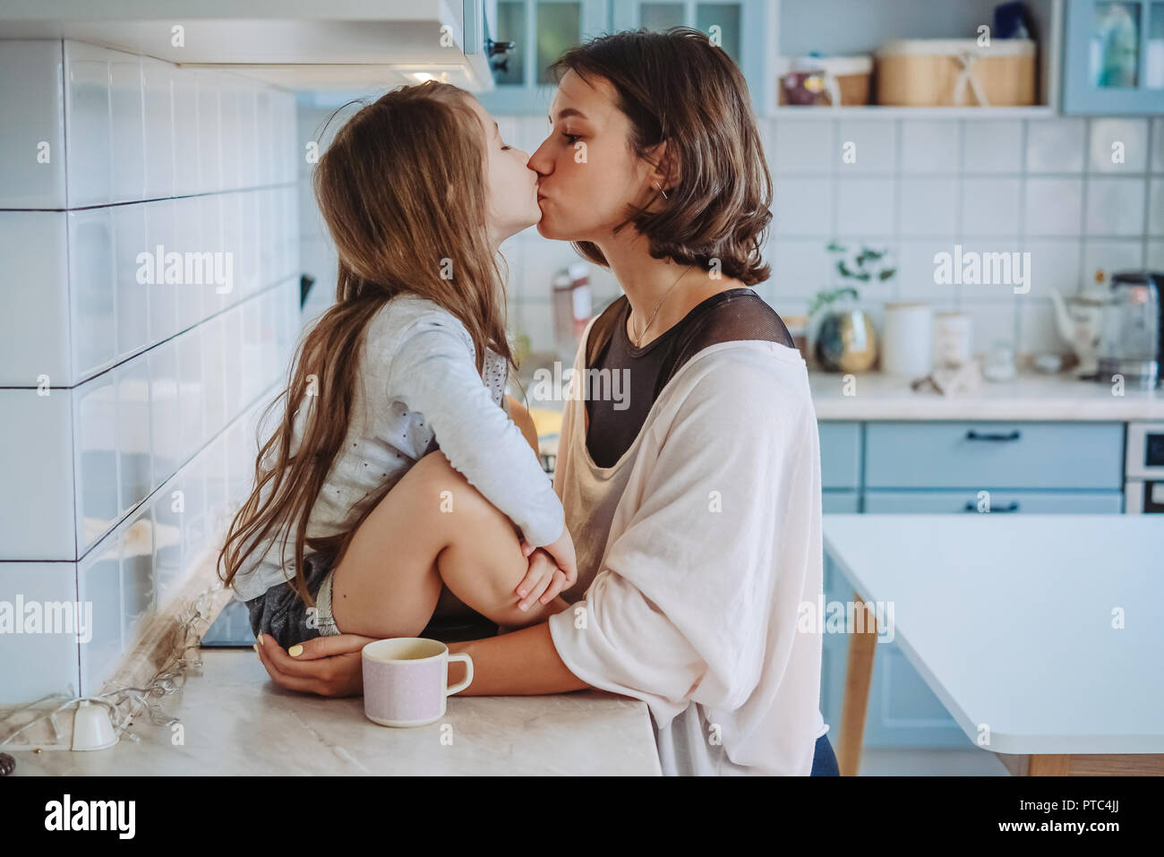 Mom kisses her little daughter in the kitchen Stock Photo - Alamy