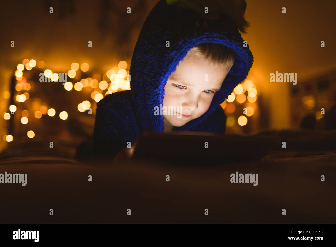 Boy in blue jacket using digital tablet against Christmas lights Stock Photo
