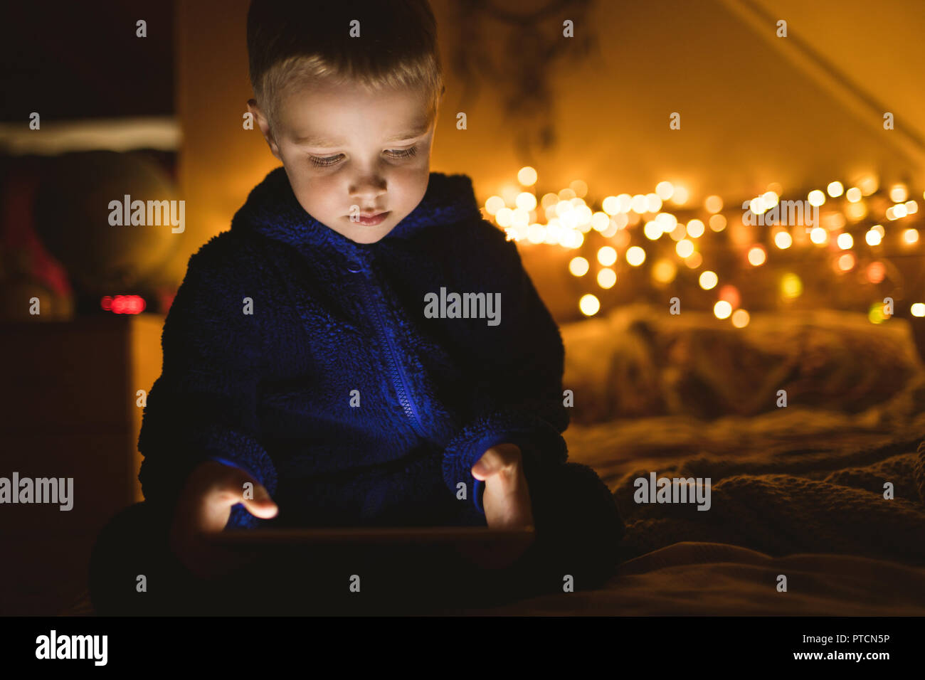 Boy in blue jacket using digital tablet against Christmas lights Stock Photo