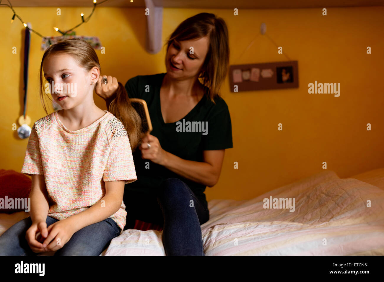 Mother combing daughters hair on bed Stock Photo