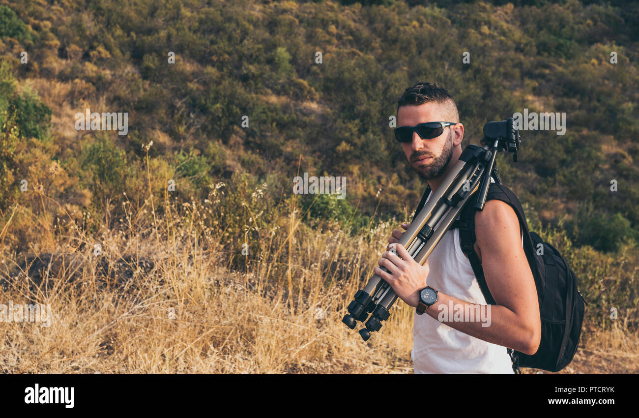 Young photographer with a beard, backpack on his back and tripod on his shoulder on the mountain Stock Photo