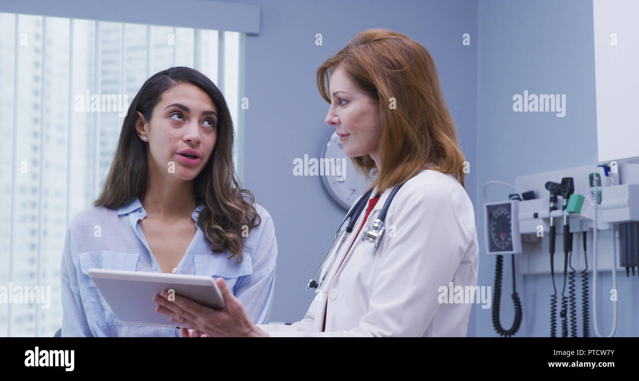 Close up of pretty hispanic woman looking at tablet device with doctor in office Stock Photo