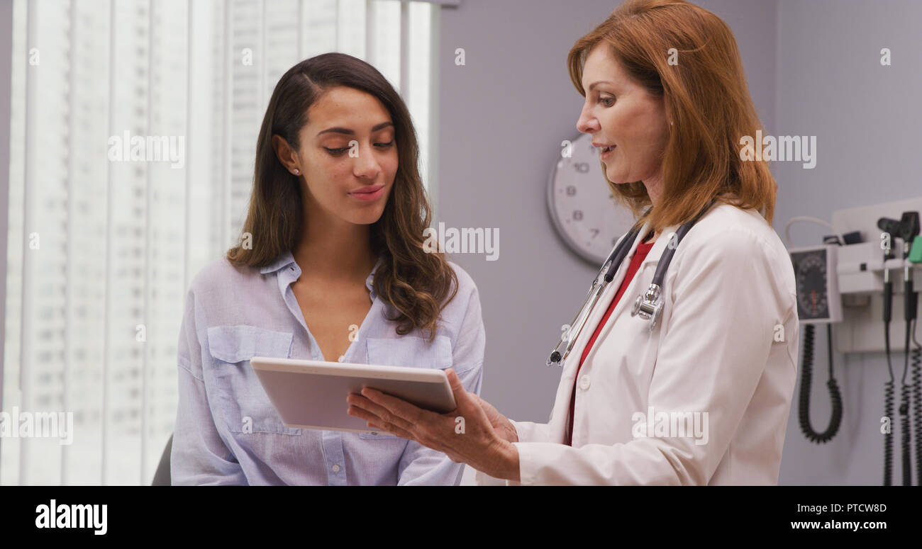Close up of mid aged doctor using tablet to review health history with patient Stock Photo
