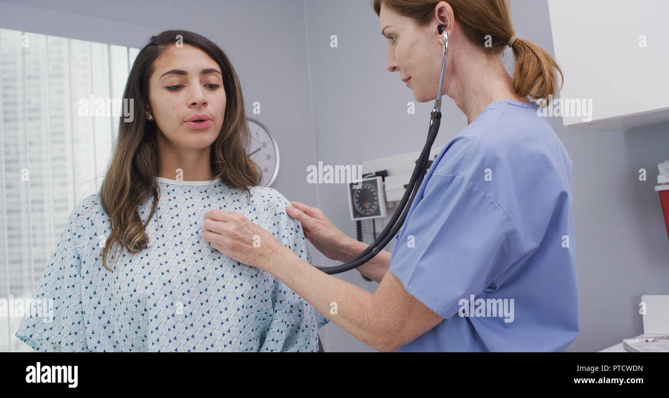 Mid aged nurse using stethoscope to examine young patients lungs and heart Stock Photo
