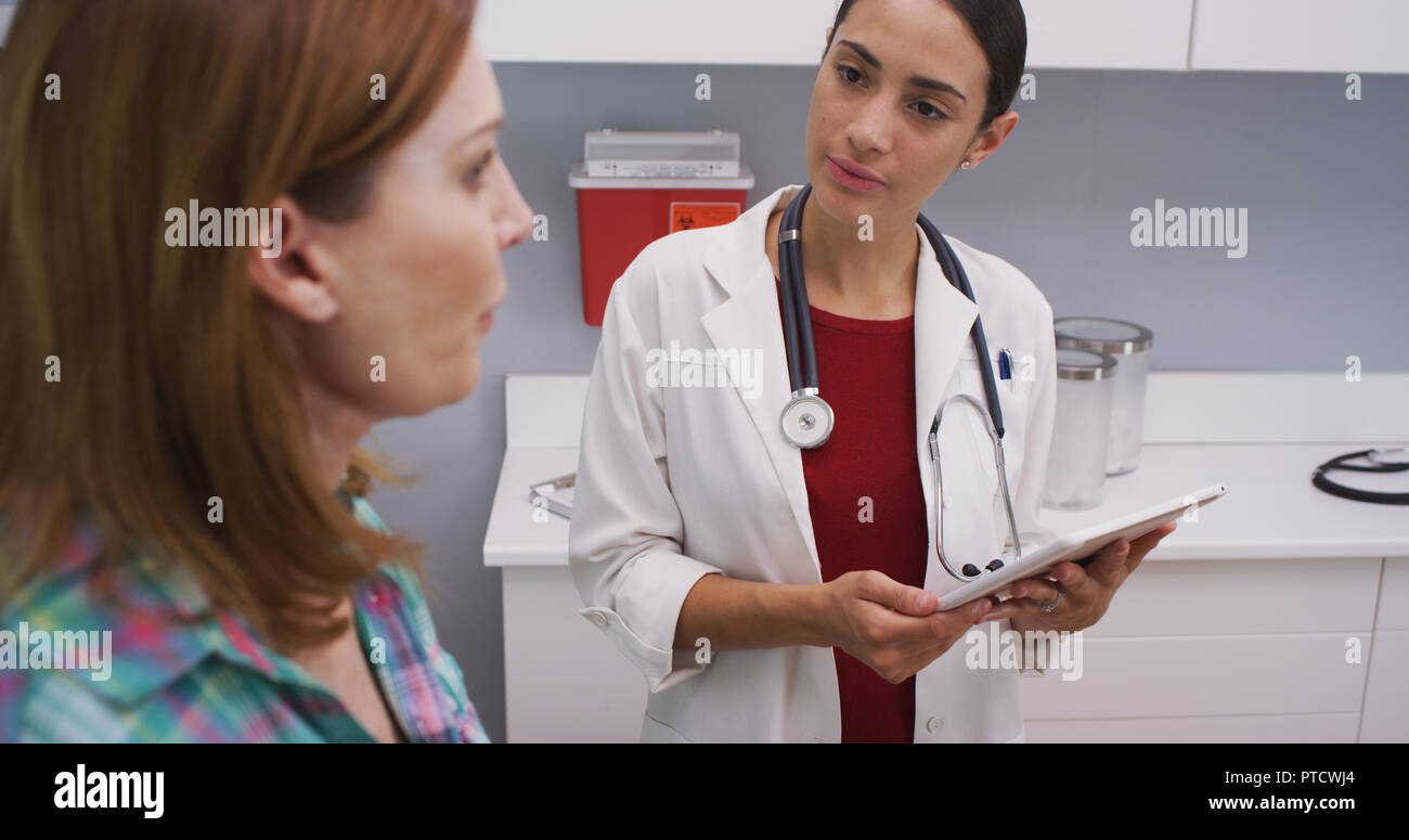 Attractive hispanic doctor using tablet to take notes of senior female patient Stock Photo