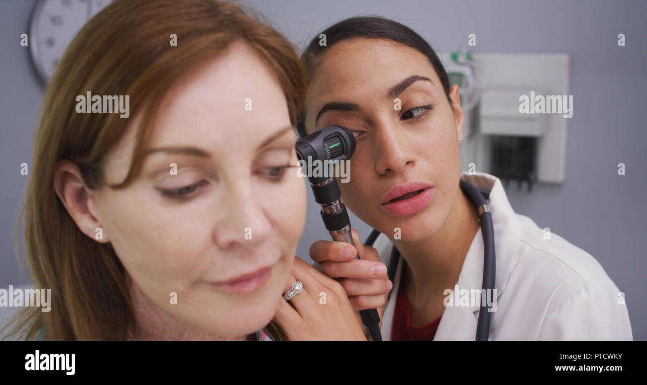 Female patient having her ear examined with otoscope by young latina doctor Stock Photo