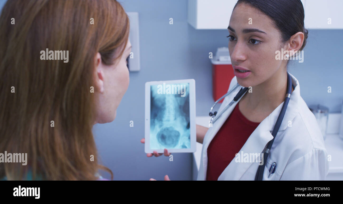 Close up of lovely latina doctor holding tablet to review patients hip x ray Stock Photo
