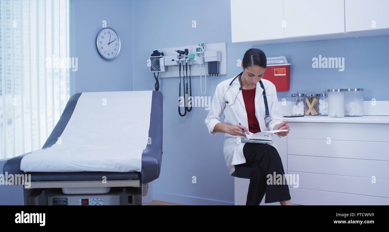 Charming young hispanic doctor reviewing notes on clipboard in hospital clinic Stock Photo