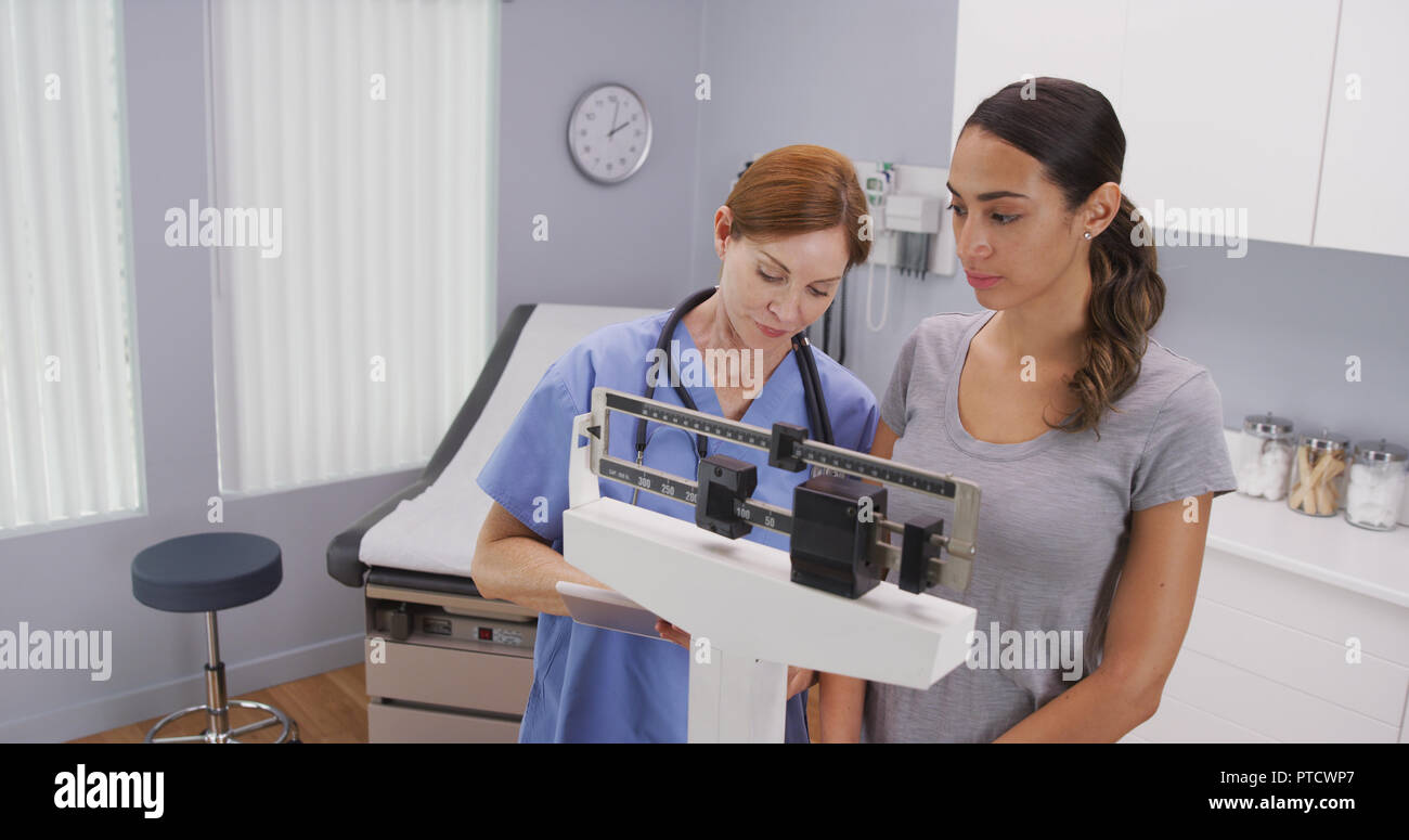 Mid aged caucasian nurse weighing female patient on scale Stock Photo