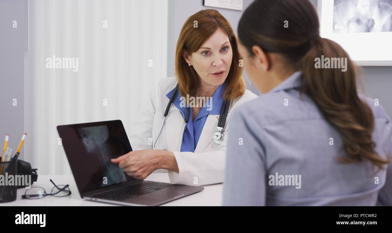 Senior doctor showing xray of spine neck and cranium to young female patient Stock Photo