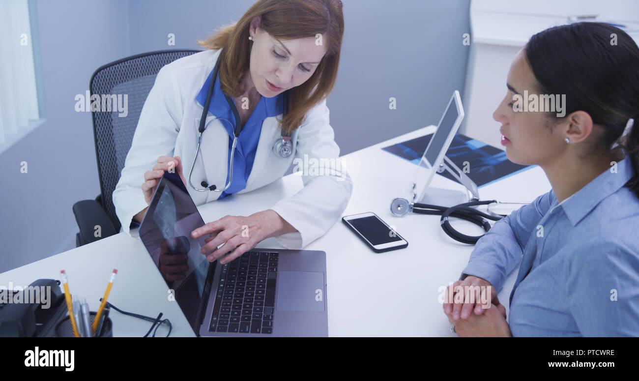 Closeup of charming old female doctor reviewing xray with young hispanic patient Stock Photo