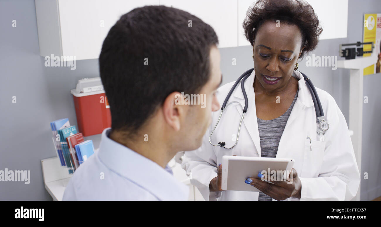 Black senior doctor using electronic notebook pad to view patient health history Stock Photo