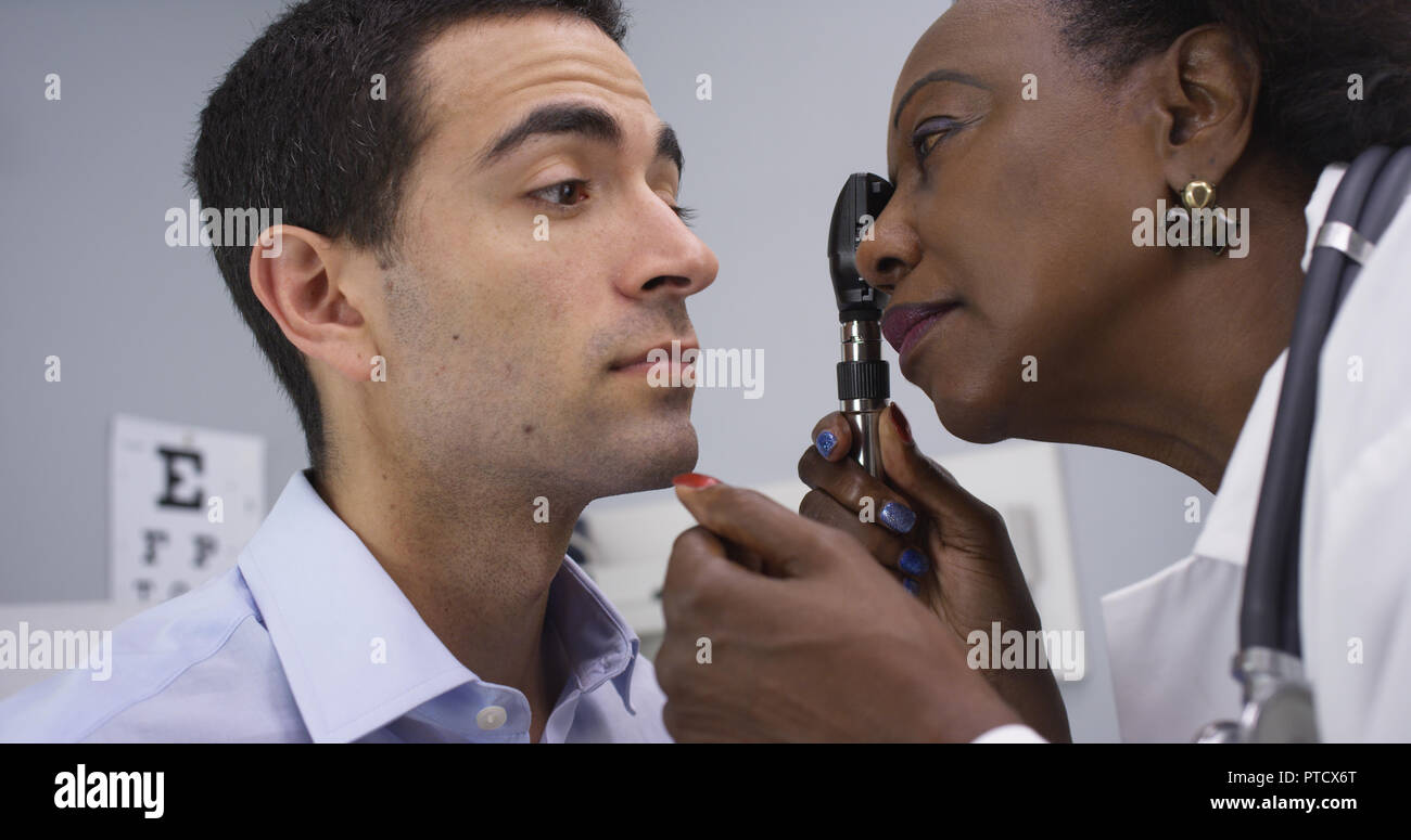 Close up of black medical doctor using retinoscope to check patients eyes Stock Photo
