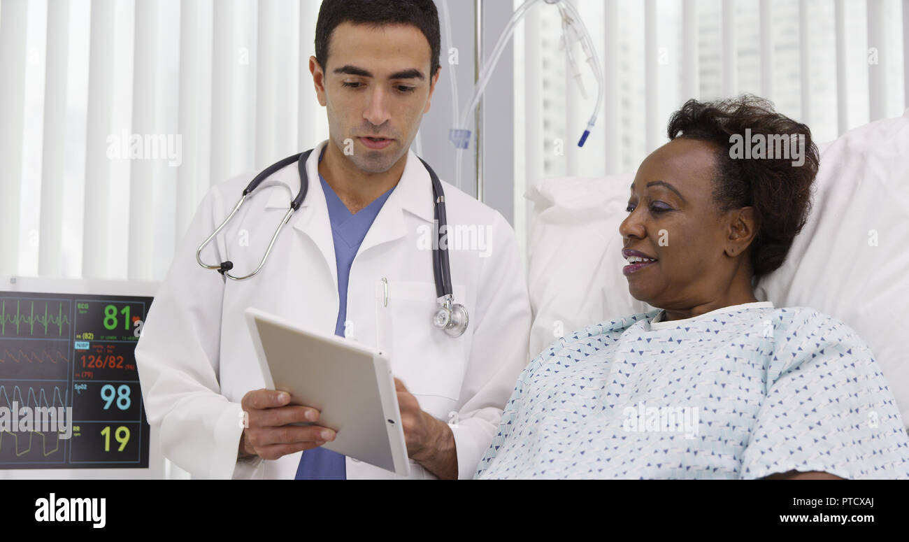 Senior black woman lying in hospital looking at portable tablet computer Stock Photo