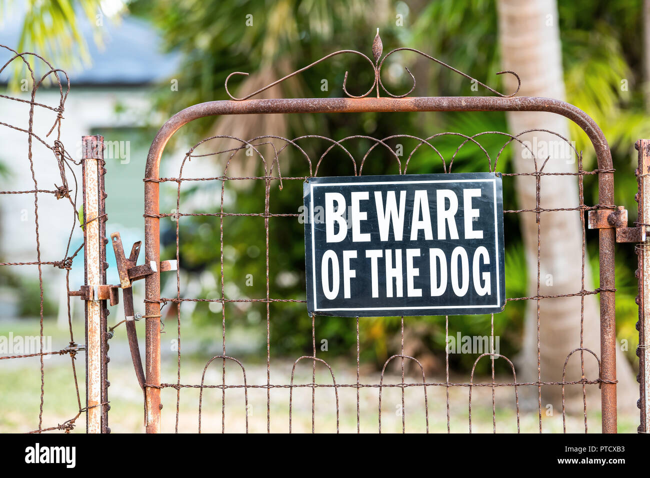Beware of the dog sign on closed rusty fence gate with rust at residential neighborhood with house, home in background and nobody Stock Photo
